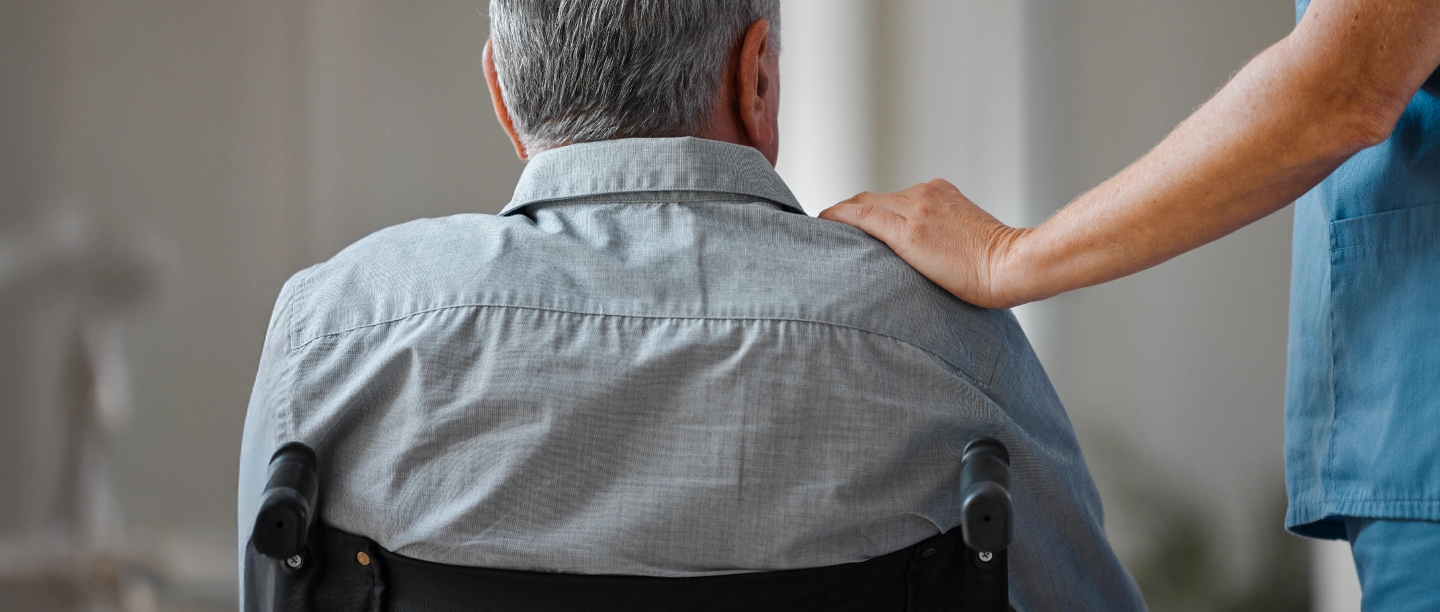 A man sits in a wheelchair with a hand on his shoulder.