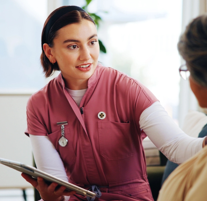 A female nurse helpfully addresses an elderly patient.